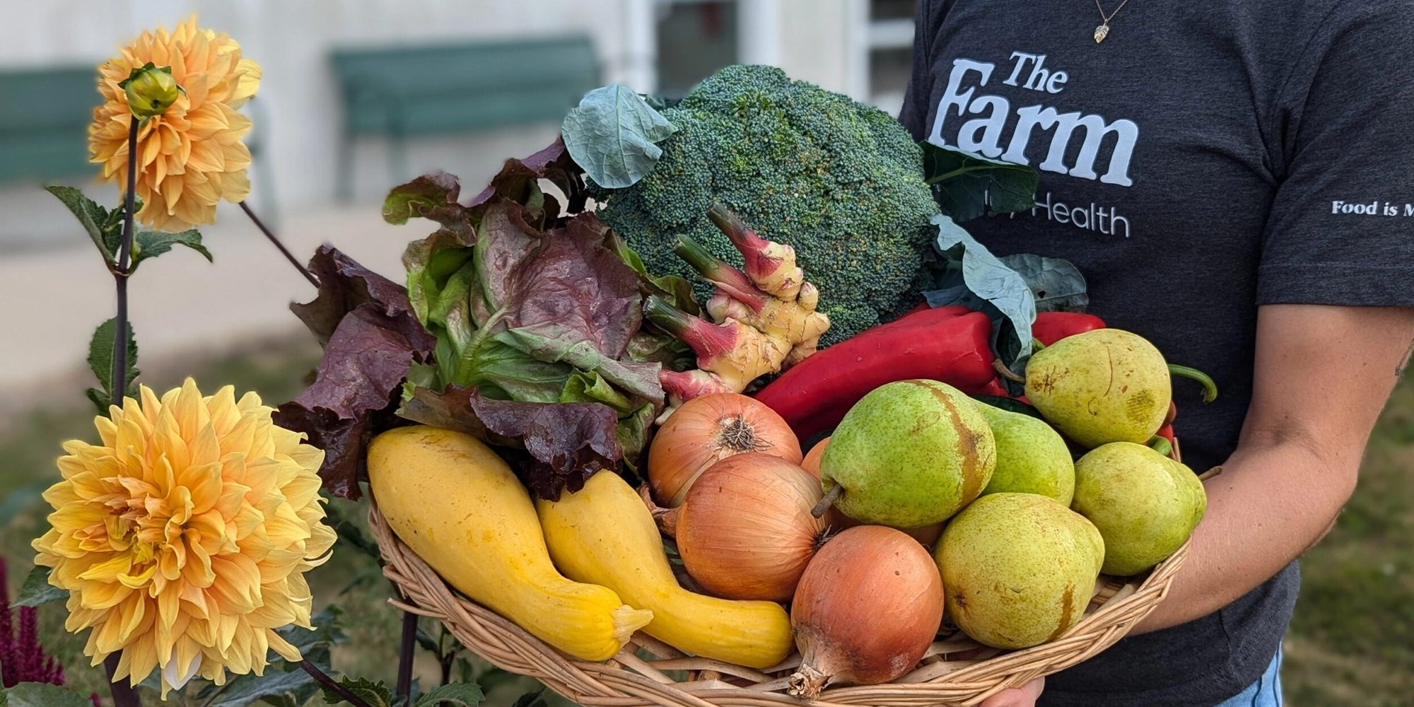 An employee of The Farm holds a large wicker basket filled with various fruits and vegetables
