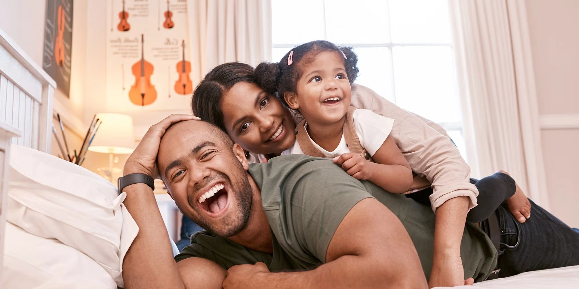 A mother, father and young daughter lie stacked on top of each other in a bed